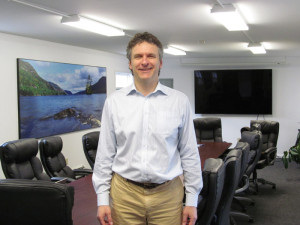 Eric Siy, executive director of the Fund for Lake George, in the non-profit environmental organization’s headquarters meeting room on Route 9 in Lake George.  Mr. Siy said images of Lake George, like the one on the left, were donated by Adirondack photographer Carl Heilman. The large flat-screen TV monitor on the right connects to a Jefferson Project station to “run the models that they’re developing for the physics, the chemistry of Lake George. It’s very educational, and it really puts eyes on the lake like we’ve never had before,” Mr. Siy said. Chronicle photo/David Cederstrom